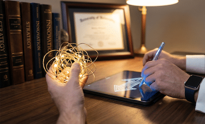 A close-up, detailed photograph of a professional's hands at a sleek wooden desk. One hand is holding a complicated, tangled knot of glowing golden wires representing confusion or complex problems. The other hand is using a futuristic, illuminated stylus tool over a tablet. On the tablet screen, the tangled wires are instantly straightening into a brilliantly bright, clear, upward-pointing arrow graphic. In the background, softly out of focus, is a stack of business books and a diploma. The lighting is warm and focused on the hands and tablet, symbolizing enlightenment and the sharpening of skills.