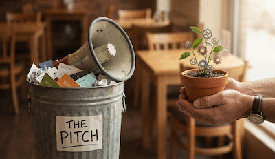 A metaphorical illustration or photo. On the left side of the frame, a pile of discarded, crumpled business cards and a megaphone are tossed into a rubbish bin labeled "THE PITCH." On the right side, two hands gently hold a small potted plant that is sprouting gears and leaves simultaneously, symbolising organic business growth and collaboration. The background is a warm, inviting cafe.